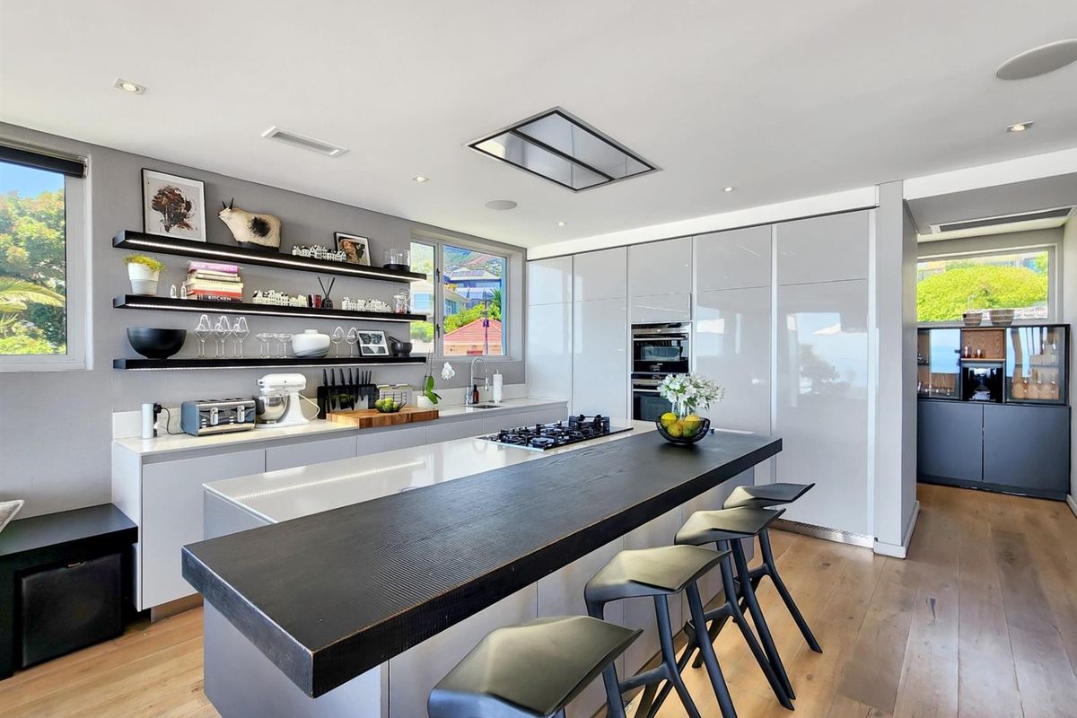 Modern kitchen featuring a large island with gas cooktop, integrated cabinetry, built-in oven, and sleek floating shelves, finished with high-quality hardwood flooring.