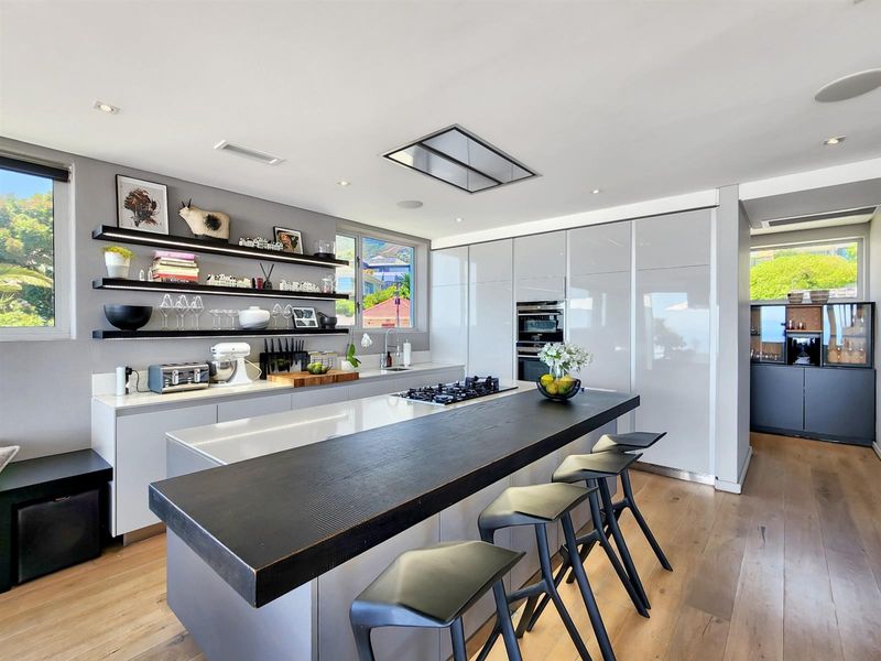 Modern kitchen featuring a large island with gas cooktop, integrated cabinetry, built-in oven, and sleek floating shelves, finished with high-quality hardwood flooring.