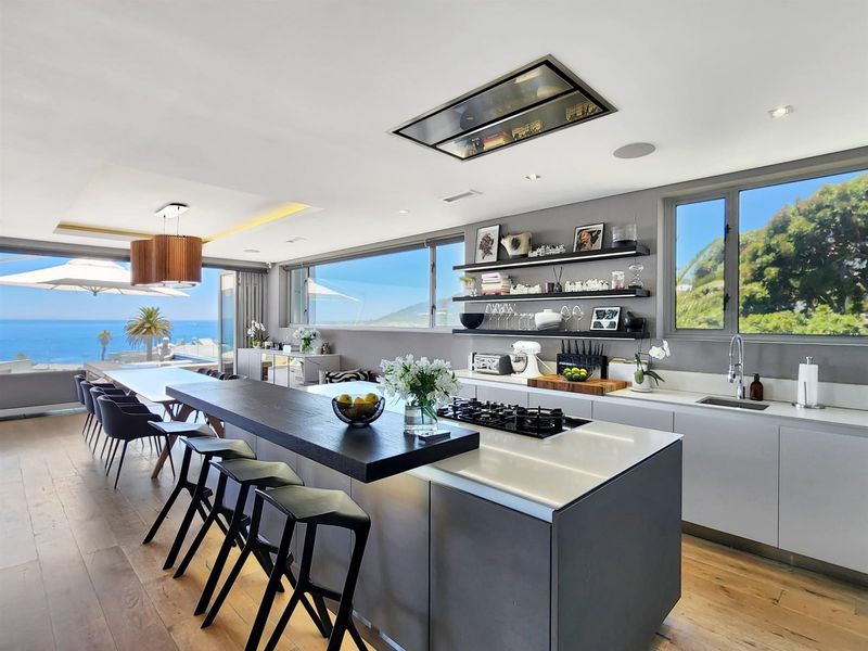 Modern open-plan kitchen and dining area featuring a large island with gas cooktop, sleek cabinetry, and expansive windows with ocean views.