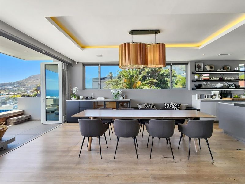 Modern open-plan living and dining area featuring timber flooring, recessed ceiling lighting, and seamless indoor-outdoor flow through large stacking glass doors.