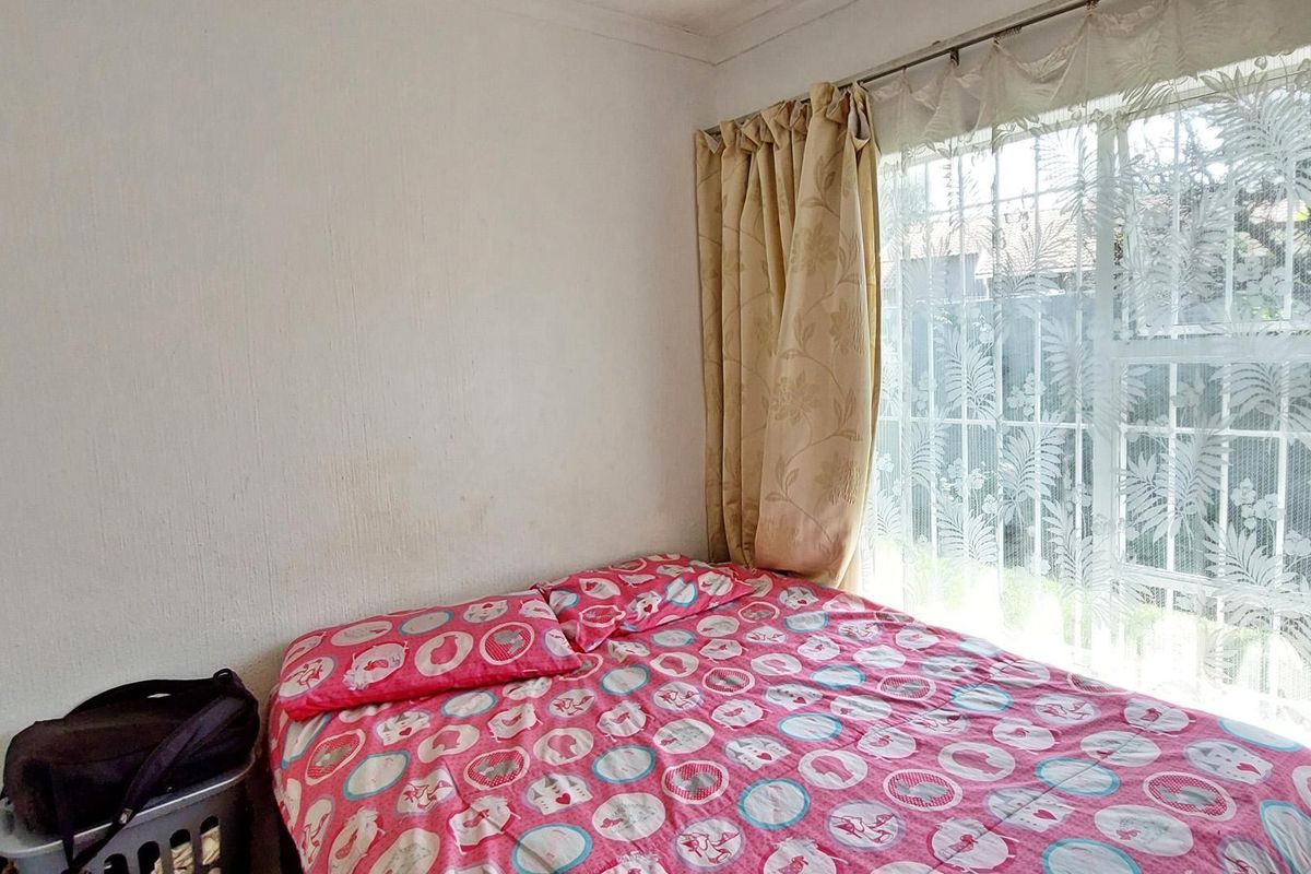 A bedroom featuring a large window with security bars and curtain rails, providing natural light.