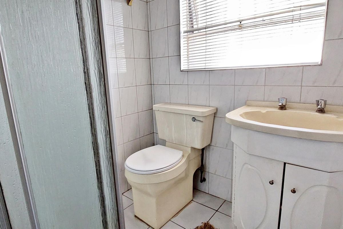 A functional bathroom featuring a shower enclosure, toilet, and vanity basin with tiled finishes throughout, currently requiring cosmetic updates.