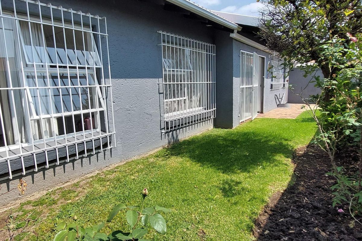 Rear exterior view of the house featuring a lawn, landscaped garden, paved walkway, and security bars on the windows and doors.