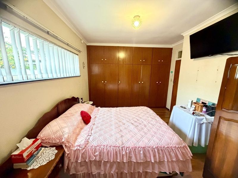 A functional bedroom featuring extensive built-in wooden cabinetry, vertical blinds, and neutral wall finishes, offering a practical layout with ample storage space.