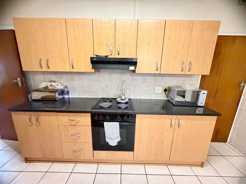 A functional kitchen featuring light wood-finish cabinetry, dark granite countertops, a built-in oven with electric hob, and a tiled backsplash.