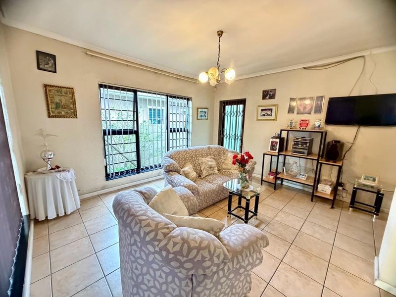 A functional living room featuring tiled flooring, security bars on windows, and a security gate, offering a neutral base for potential interior updates.