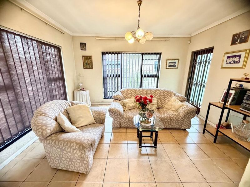 A living room featuring ceramic floor tiles, vertical blinds, and a security gate, offering a functional space with potential for modern updates.