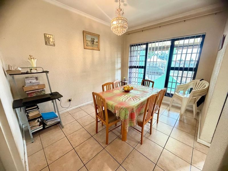 A dining room featuring tiled flooring, a crystal chandelier, and large windows fitted with security bars, providing natural light to the space.