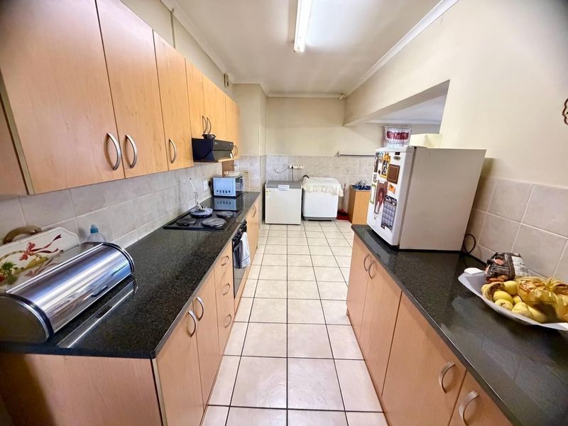 A functional galley-style kitchen featuring light wood cabinetry, dark granite countertops, tiled flooring, and a built-in hob and oven.