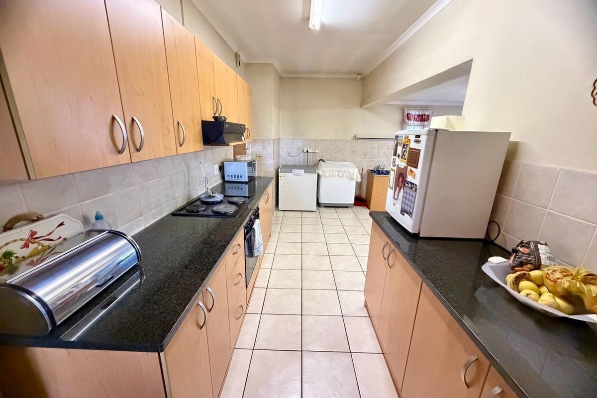 A functional galley-style kitchen featuring light wood cabinetry, dark granite countertops, tiled flooring, and a built-in hob and oven.