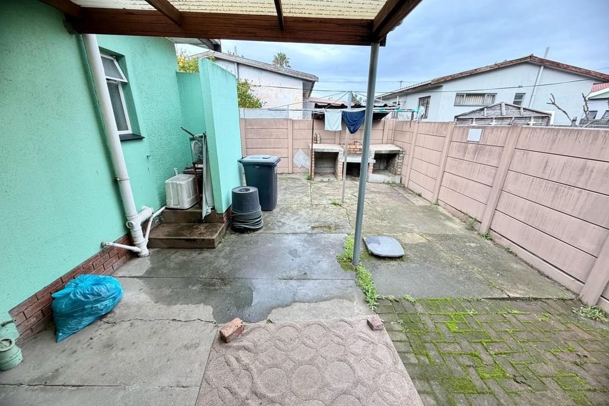 Rear courtyard featuring a covered patio area, built-in braai, and paved flooring, offering potential for outdoor entertainment space improvement.