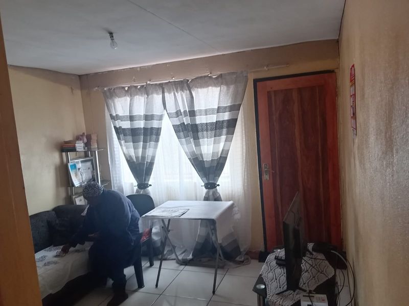 A living room space featuring tiled flooring and a timber door, currently showing signs of wear including peeling paint and wall surface deterioration.