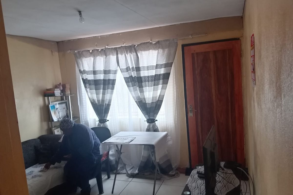 A living room space featuring tiled flooring and a timber door, currently showing signs of wear including peeling paint and wall surface deterioration.