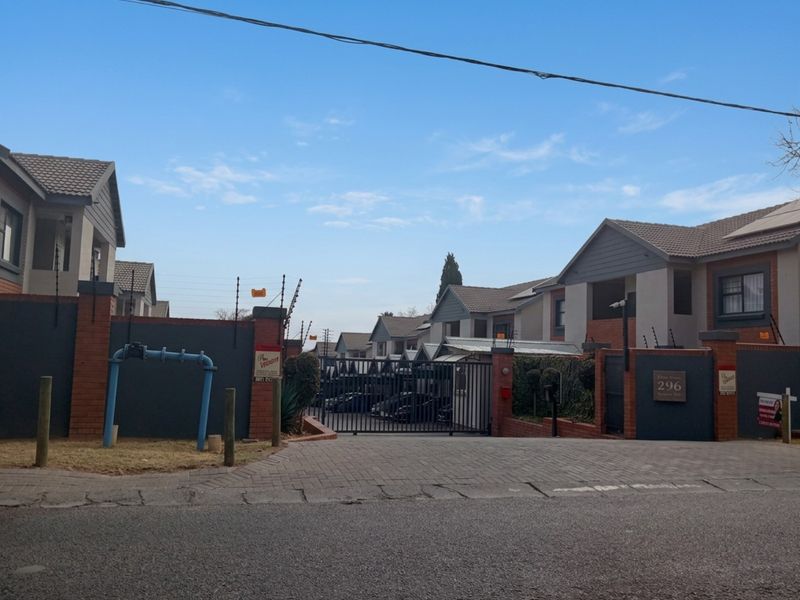 Street view of the apartment complex entrance featuring secure gated access, brick paving, and perimeter electric fencing.