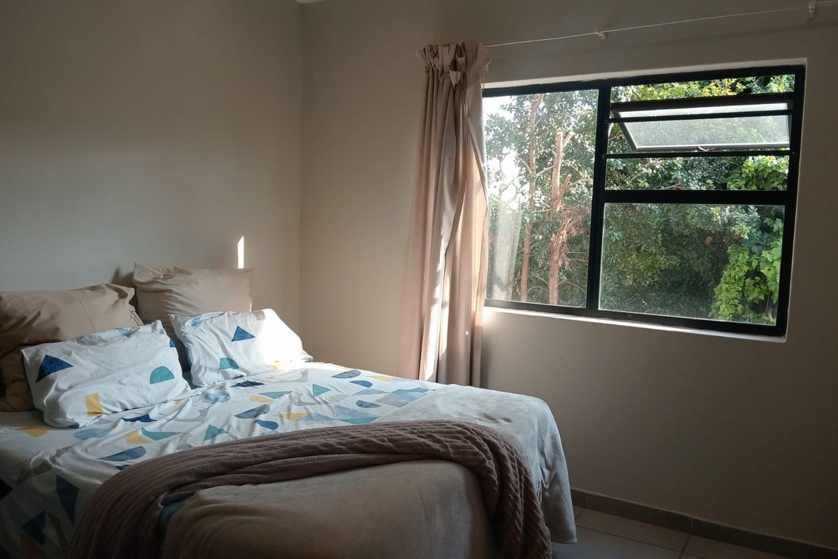 A bedroom featuring tiled flooring and a large aluminium-framed window with a curtain rail, offering a view of the surrounding greenery.