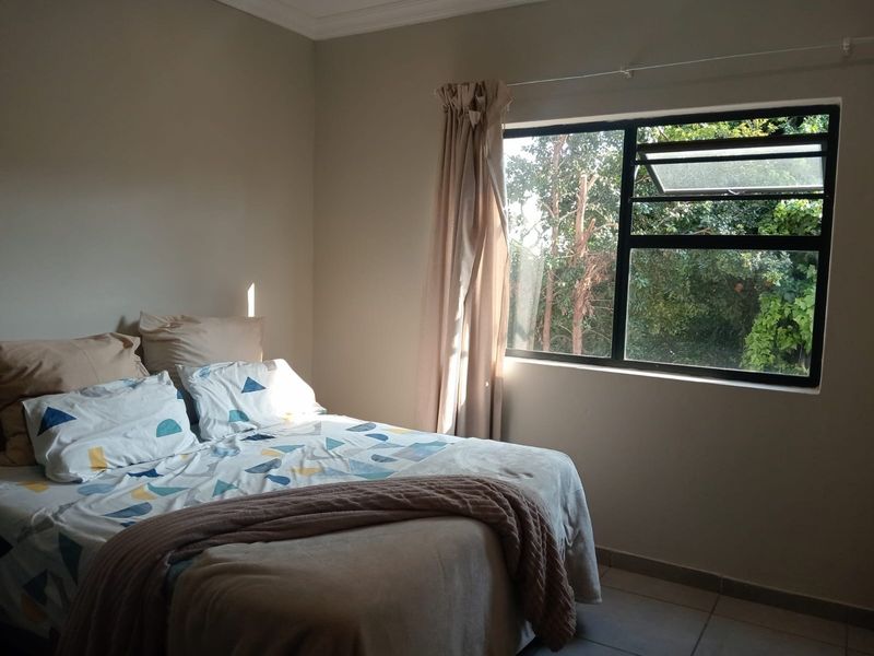 A bedroom featuring tiled flooring and a large aluminium-framed window with a curtain rail, offering a view of the surrounding greenery.