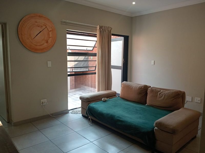 A living room featuring tiled flooring, recessed downlighting, and a sliding glass door providing access to an outdoor area with security bars.