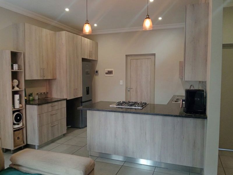 Modern kitchen featuring light wood-grain cabinetry, granite countertops, a gas hob, and tiled flooring with integrated lighting.