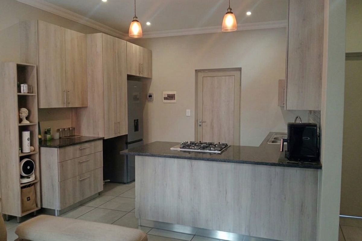 Modern kitchen featuring light wood-grain cabinetry, granite countertops, a gas hob, and tiled flooring with integrated lighting.