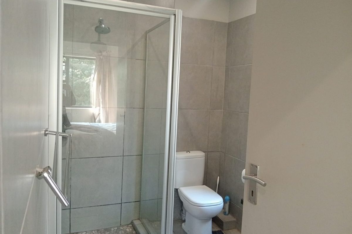 A functional bathroom featuring a glass-enclosed shower with a pebble floor base and a standard toilet with neutral wall tiling.