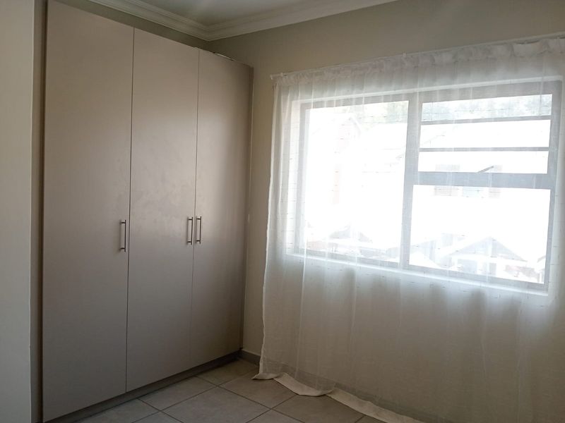 A bright, empty bedroom featuring neutral tiled flooring and built-in cupboards, offering a clean canvas for personalization.
