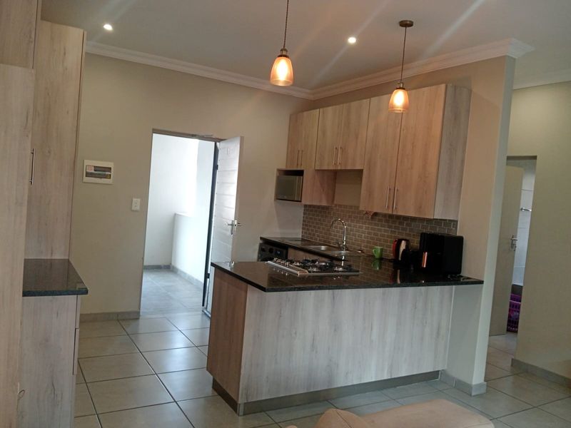 Modern kitchen featuring light wood-finish cabinetry, granite countertops, a gas hob, and a tiled backsplash, with an open-plan layout and direct balcony access.