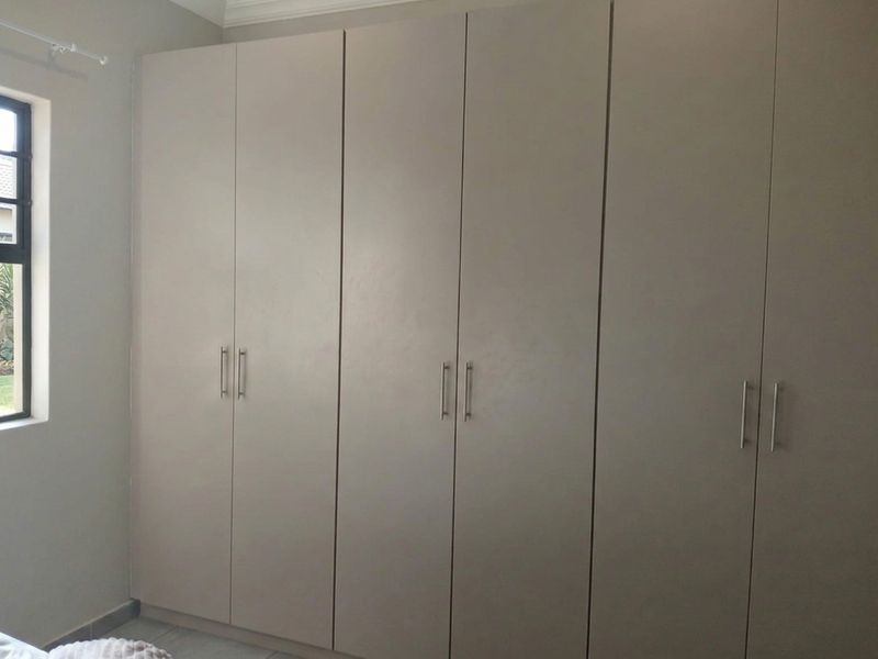 A bedroom featuring neutral-toned built-in cupboards with modern handles and a window providing natural light.
