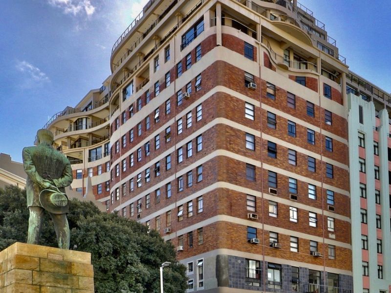 A multi-story apartment building featuring a brick facade, multiple balconies, and ground-level commercial space, situated in an urban setting.