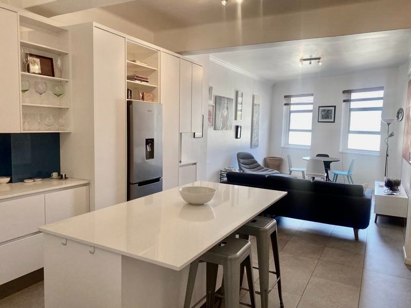 Modern open-plan living area featuring a sleek kitchen with a central island, quartz countertops, ample built-in cabinetry, and neutral tiled flooring throughout.