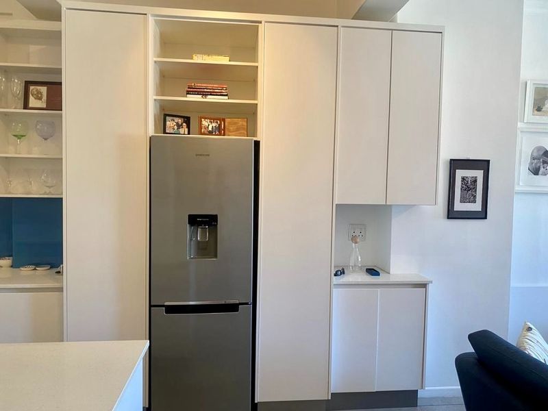 A modern kitchen featuring white built-in cabinetry, quartz countertops, and an integrated stainless steel refrigerator with open shelving for display.