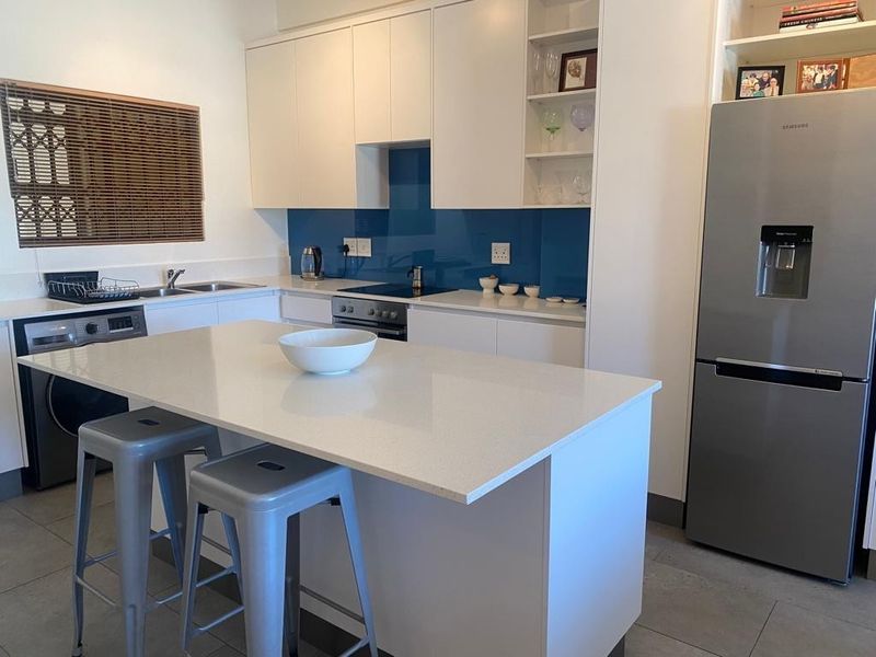 Modern kitchen featuring white cabinetry, a central quartz island, blue glass splashback, and integrated appliances, offering a clean and functional cooking space.