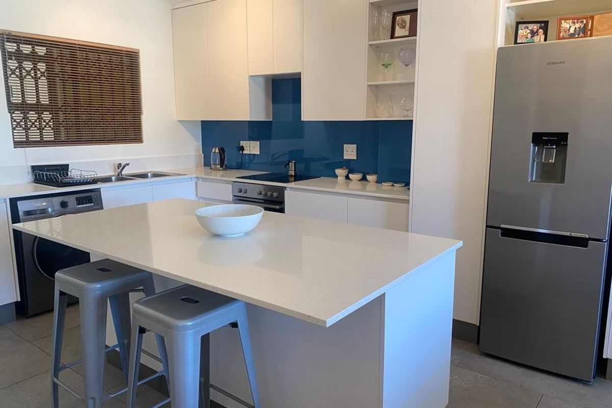 Modern kitchen featuring white cabinetry, a central quartz island, blue glass splashback, and integrated appliances, offering a clean and functional cooking space.