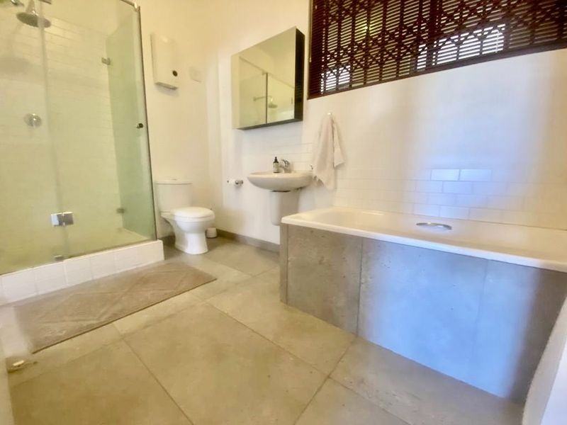 A functional bathroom featuring a glass-enclosed shower, a pedestal sink, a bathtub with a concrete-style surround, and large format floor tiles.
