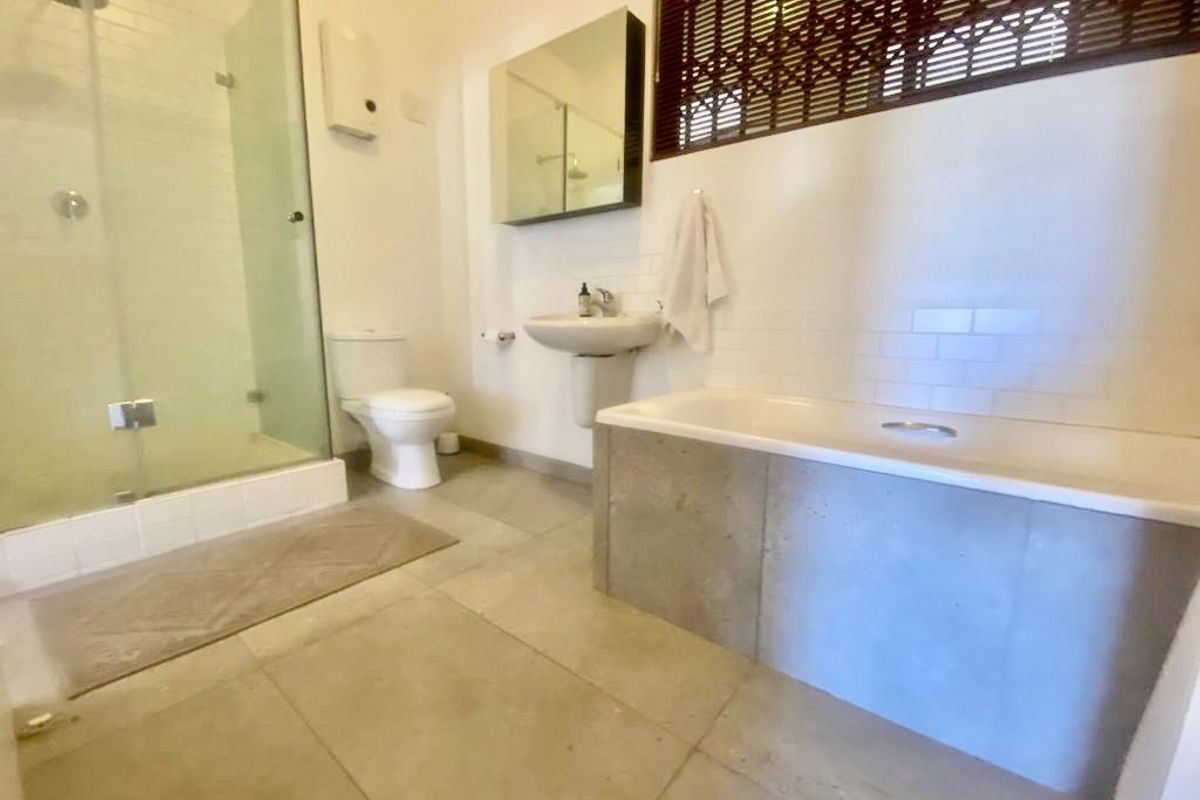 A functional bathroom featuring a glass-enclosed shower, a pedestal sink, a bathtub with a concrete-style surround, and large format floor tiles.