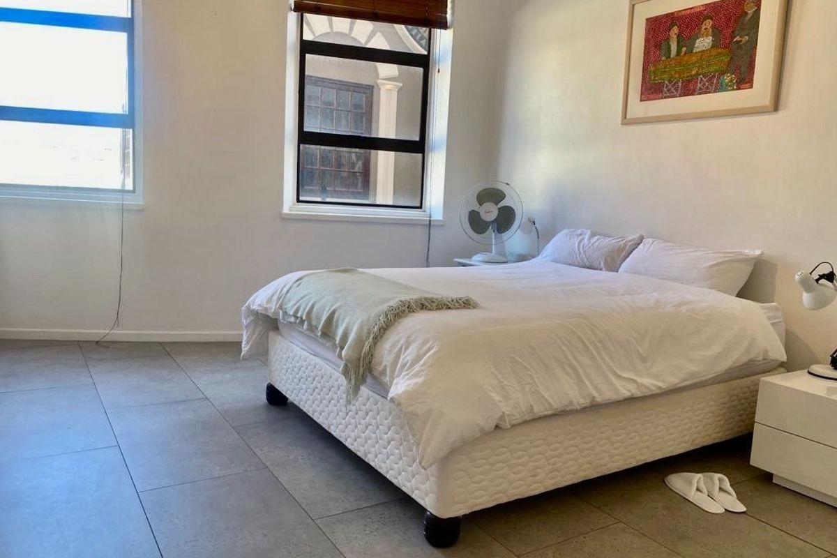 A bright bedroom featuring large windows with venetian blinds and neutral tiled flooring, offering a clean and functional living space.