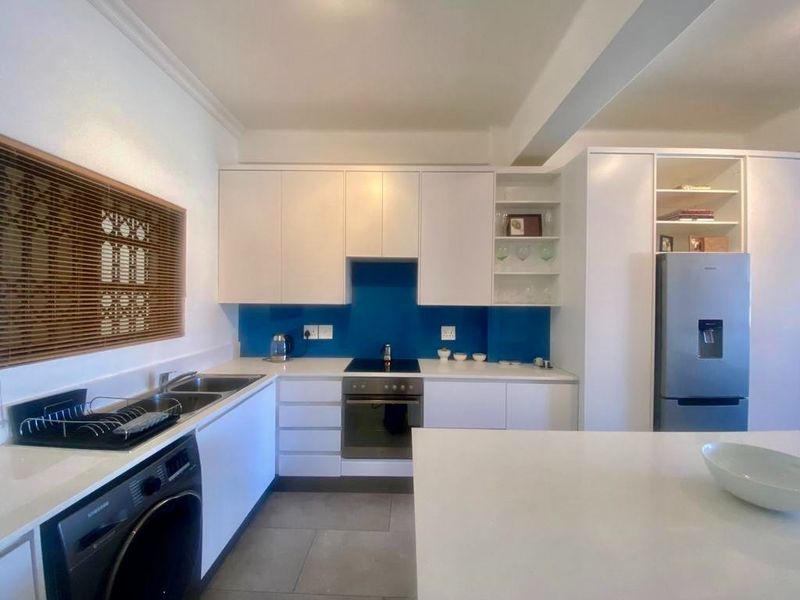 Modern kitchen featuring white cabinetry, stone countertops, a blue glass splashback, integrated oven and hob, and tiled flooring.