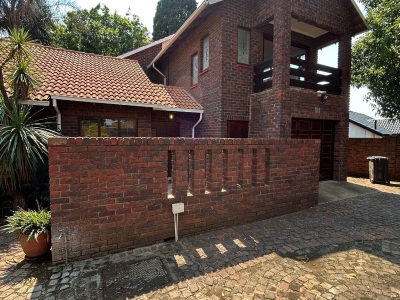 A double-story face brick house featuring a tiled roof, a front balcony, and a paved driveway with a brick boundary wall.