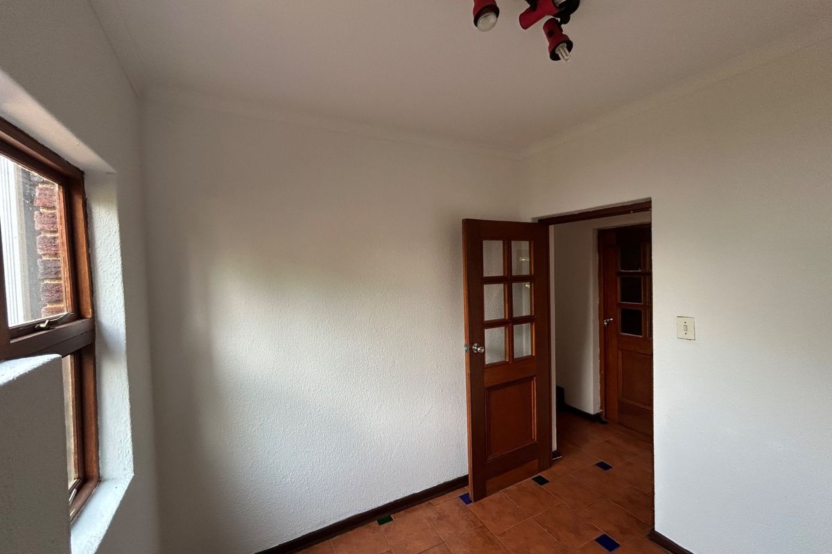 An empty bedroom featuring tiled flooring, wooden doors, and a window, providing a blank canvas for potential interior design updates.