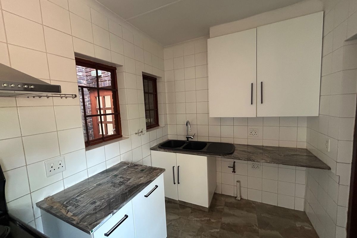 A clean, functional kitchen featuring white cabinetry, dark laminate countertops, a double sink, and tiled splashbacks with an extractor fan.