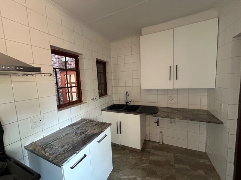 A clean, functional kitchen featuring white cabinetry, dark laminate countertops, a double sink, and tiled splashbacks with an extractor fan.