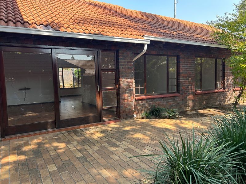 Rear view of a facebrick house featuring a paved patio area, terracotta tiled roof, and large sliding glass doors providing access to the interior.