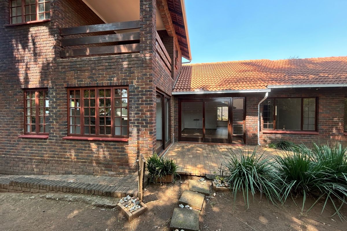 Rear view of a double-story face brick house featuring a paved patio, upper balcony, and timber-framed windows.