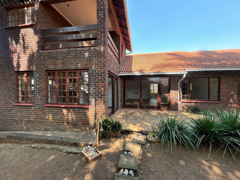 Rear view of a double-story face brick house featuring a paved patio, upper balcony, and timber-framed windows.