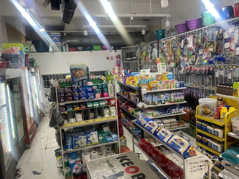 A commercial retail space featuring tiled flooring, wire mesh shelving, and commercial refrigeration units, currently utilized as a convenience store.