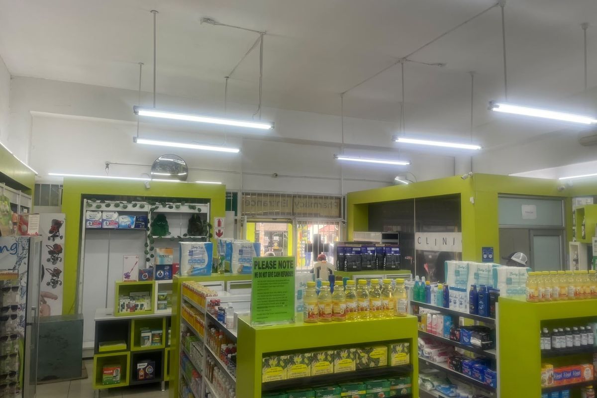 Interior view of a commercial pharmacy space featuring built-in shelving units, fluorescent lighting, and tiled flooring.