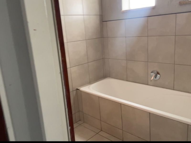 A functional bathroom featuring a built-in bathtub with neutral wall and floor tiling and a chrome mixer tap.