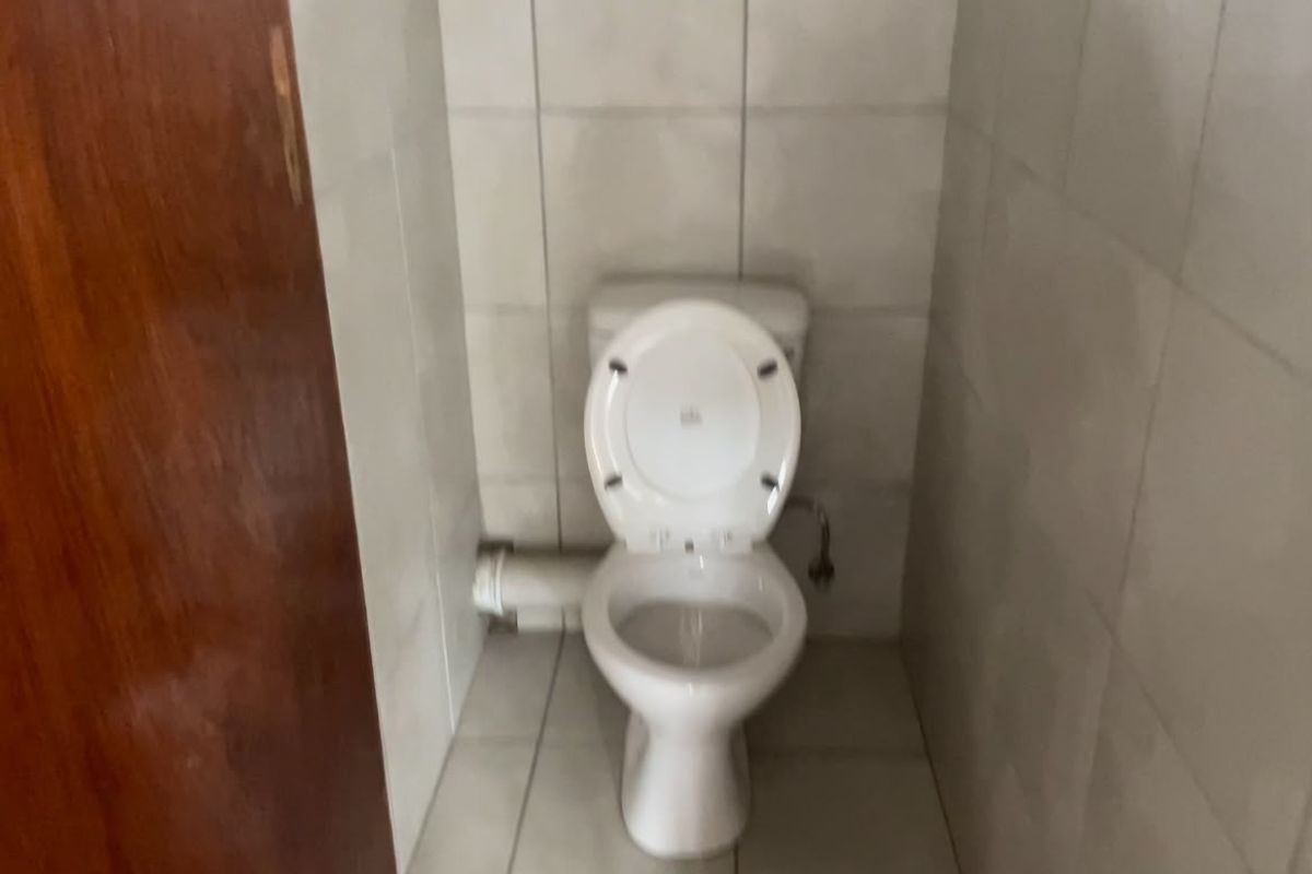 A small, functional bathroom featuring a standard toilet and tiled surfaces, currently showing signs of dated finishes and exposed plumbing.