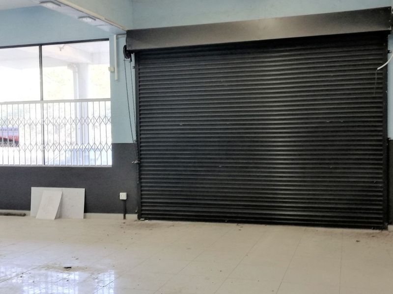 Spacious commercial utility area featuring a large roller shutter door, tiled flooring, and secure aluminium window frames with security gates.