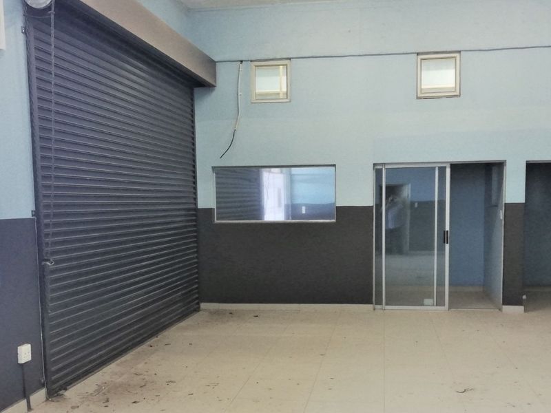 A spacious commercial utility area featuring a large roller shutter door, tiled flooring, and multiple glass-paneled access points for versatile business use.