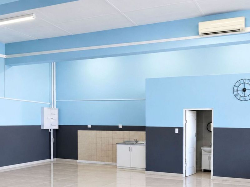 Spacious open-plan commercial area featuring tiled flooring, dual air conditioning units, and a compact kitchenette with built-in cabinetry and sink.